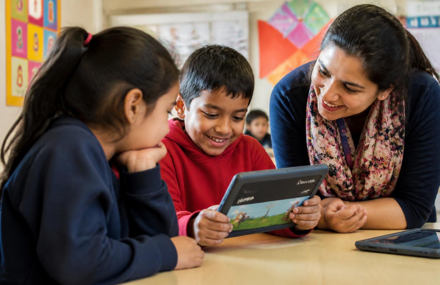 Children sharing a tablet with an Owl Core literacy app while a teacher helps